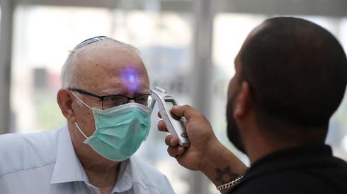 Un hombre mayor procede a tomarse la temperatura en un hospital de Tel Aviv