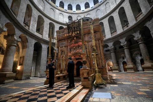 Un sacerdote ortodoxo griego y un cuidador se paran frente al edículo desierto en la Iglesia del Santo Sepulcro en la Ciudad Vieja de Jerusalem. 