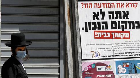 Un residente de Bnei Brak se encuentra al lado de un cartel que insta a los residentes a quedarse en casa. 