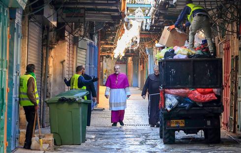 El Arzobispo Pierbattista Pizzaballa pasa junto a los recolectores de basura en la Ciudad Vieja de Jerusalén mientras se dirige a la Iglesia del Santo Sepulcro para el servicio del Domingo de Pascua, 12 de abril de 2020. 