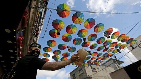 Un trabajador palestino con una máscara en el sur de la Franja de Gaza rocía agua afuera de las tiendas decoradas para el Ramadán. 