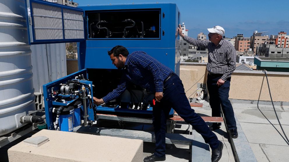 El ingeniero palestino Raed Nakhal del Fondo de Ayuda para Niños de Palestina, a la derecha, y el ingeniero Abdullah Dewik, comprueban la máquina GEN-M que genera agua potable segura desde el techo del hospital pediátrico al-Rantisi en la ciudad de Gaza. 