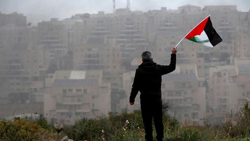 Un palestino agita una bandera frente a un asentamiento judío en Judea y Samaria. 