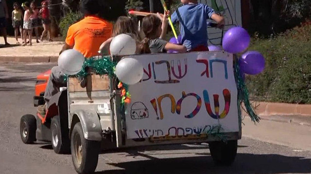 Niños en un tractor desean una fiesta feliz por las calles de Ramot Naftalí. 
