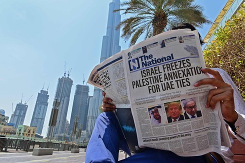 Un hombre lee el diario “The National” con la torre Burj Khalifa de Dubai de fondo. 
