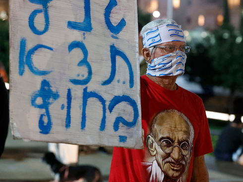 Un hombre protesta en Tel  Aviv, con barbijo y remera con la imagen del Mahatma Gandhi. 