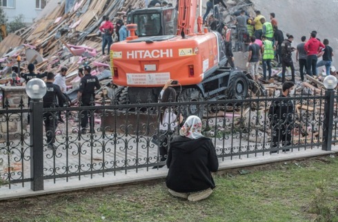 Una mujer reza mientras los rescatistas trabajan sobre los escombros.