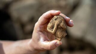 Pequeña piedra tallada con la figura de una mujer que toca un tambor. 