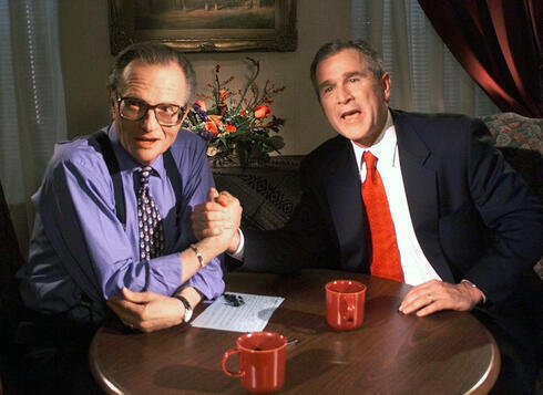 Larry King bromea con el candidato presidencial republicano George W. Bush después de terminar una entrevista, en diciembre de 1999.