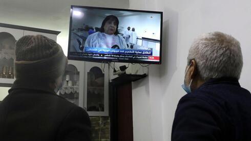 Los palestinos miran la transmisión de televisión en vivo de la ministra de Salud palestina, Mai al-Kaila, anunciando el lanzamiento de la campaña de vacunación contra el COVID-19 en la ciudad de Hebrón, en Cisjordania.