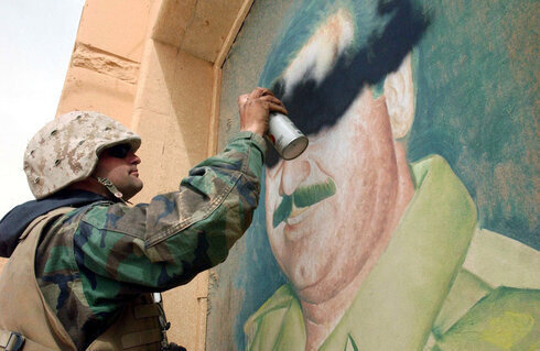Un soldado estadounidense pinta sobre la imagen de Saddam Hussein en 2003.