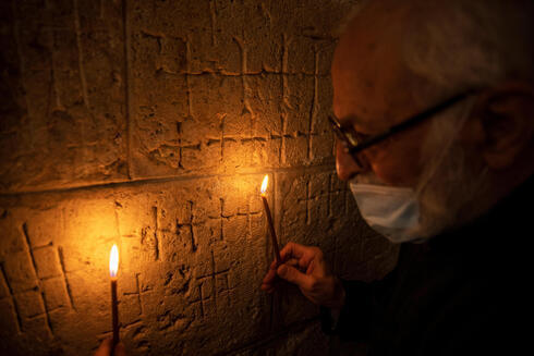 El padre Samuel Aghoyan, el superior armenio de la Iglesia del Santo Sepulcro, sostiene velas para iluminar las cruces grabadas en el antiguo muro de piedra de la capilla de Santa Elena. (Reuters) Las cruces grabadas en el antiguo muro de piedra de la capilla de Santa Elena en Iglesia del Santo Sepulcro en Jerusalem.