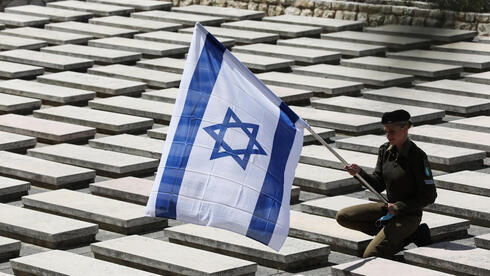 Una soldada del Ejército de Israel sostiene una bandera entre las tumbas del cementerio militar Monte Herzl. 