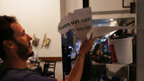 Un comerciante israelí quita un cartel: "Obligatorio el uso de máscarilla". (Moti Kimchi) Barbijo Cartel