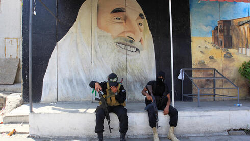 Combatientes de Hamas frente a un mural que representa al fundador de Hamas, Ahmed Yassin. 