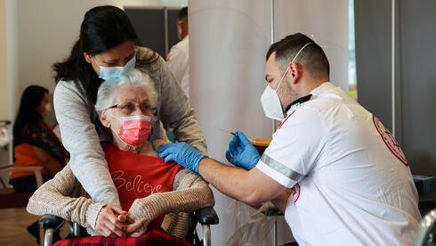 Una adulta mayor de una residencia de ancianos en Netanya sostiene la mano de su cuidador mientras recibe la vacuna contra el coronavirus.