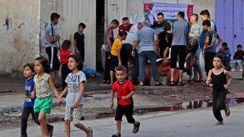 Niños pasean por una calle de Gaza, mientras a sus espaldas sacrifican a un animal en ocasión de Eid Al Adha. (AFP) Gaza Niños Sacrificio