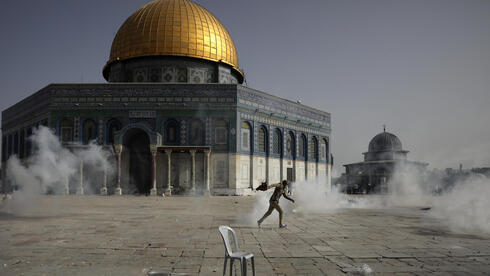 Um palestino foge de gás lacrimogêneo durante confrontos com as forças de segurança israelenses em frente ao Domo da Rocha na mesquita de Al Aqsa.