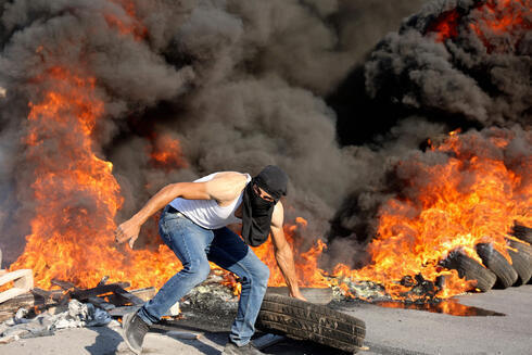 Un alborotador palestino delante de unos neumáticos ardiendo durante los enfrentamientos con las fuerzas israelíes cerca de Beita.