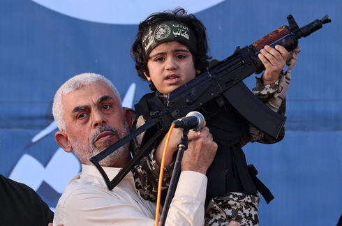 Yahya Sinwar, líder de Hamás, sostiene a un niño con una ametralladora en un acto público. 