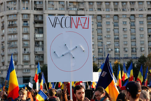 Hombre sujetando pancarta con jeringas en forma de esvástica durante una manifestación contra las nuevas medidas de salud en Rumania. 