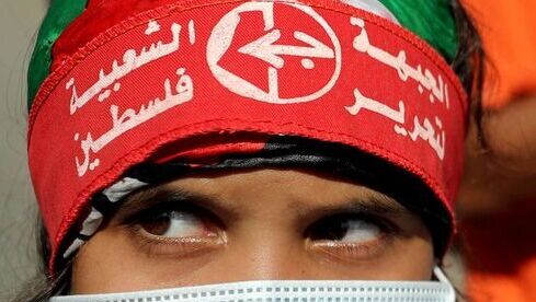 Una niña con una máscara protectora y la cinta de la cabeza del Frente Popular para la Liberación de Palestina (FPLP) mira durante una manifestación en Gaza.
