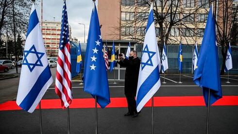 Un guardia albanés toma fotos de la bandera de Israel, de Estados Unidos y de Kosovo expuestas durante una ceremonia en la sede del Ministerio de Asuntos Exteriores en Pristina, el 1 de febrero de 2021.