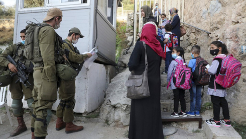 Estudiantes y profesores palestinos esperan a que los soldados israelíes les permitan cruzar un puesto de control militar cerca del asentamiento judío de Beit Hadassa. 