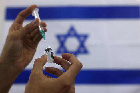 Una dosis de vacuna contra el COVID-19. De fondo, la bandera israelí. 