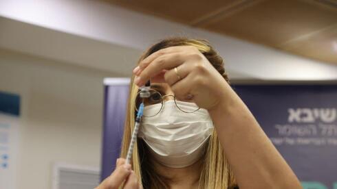 Una enfermera prepara una inyección de la cuarta dosis para aplicar a población de riesgo. 
