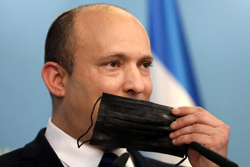 El primer ministro Naftalí Bennett sostiene una mascarilla durante una conferencia de prensa sobre la situación del COVID-19 en Israel. 