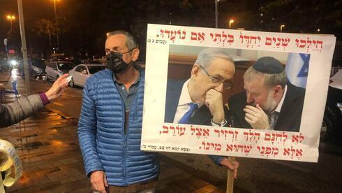 Un manifestante contra el acuerdo sostiene un cartel con una foto en la que se ve al ex primer ministro junto al fiscal general Mandelblit. 