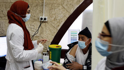 Un trabajador médico palestino junto a un hombre que espera recibir una vacuna contra el COVID-19 en Jerusalem Este.