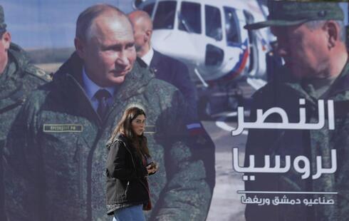 Una mujer pasa junto a una valla publicitaria que muestra al presidente ruso Vladimir Putin en Damasco. 