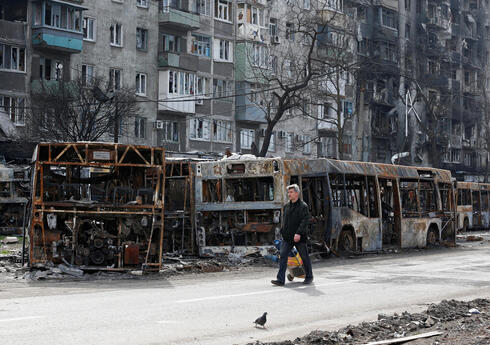 Un civil camina junto a autobuses carbonizados en medio del asedio ruso a Mariupol.