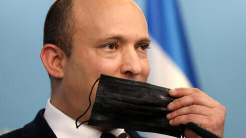 El primer ministro Naftalí Bennett sostiene una máscara facial durante una conferencia de prensa sobre la situación de COVID-19 en Israel. 