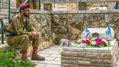 Un soldado sentado junto a una tumba en un cementerio militar. 