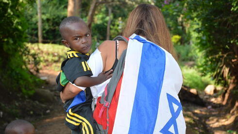 Una voluntaria atiende a un huerfanito envuelta en una bandera de Israel. 