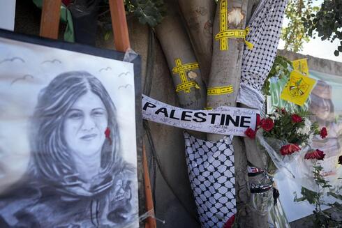 La cinta amarilla marca los agujeros de bala, y un retrato y flores crean un monumento improvisado en el sitio donde fue asesinada la periodista Shireen Abu Akleh. 