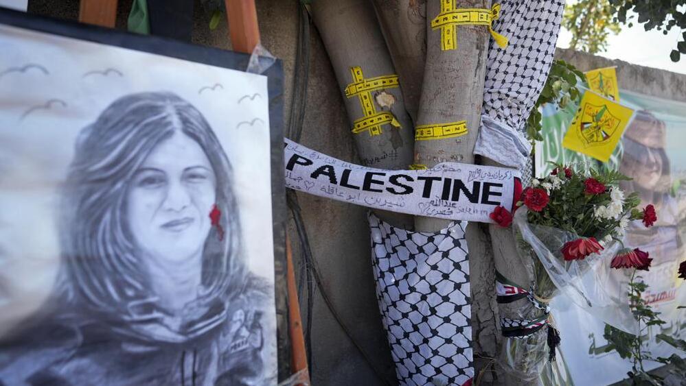 La cinta amarilla marca los agujeros de bala, y un retrato y flores crean un monumento improvisado en el sitio donde fue asesinada la periodista Shireen Abu Akleh. 