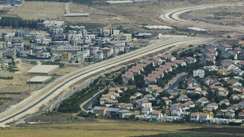 Una vista aérea muestra una aldea palestina, a la izquierda, y un asentamiento, a la derecha, separados por el muro de separación en Cisjordania.