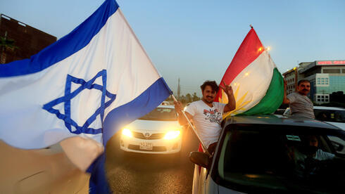 Una manifestante kurdo asoma por la ventanilla de un auto con una bandera kurda y otra israelí. 