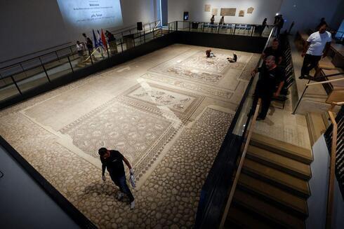 Los trabajadores limpian un mosaico de la época romana restaurado después de ser expuesto en su emplazamiento original en Lod.