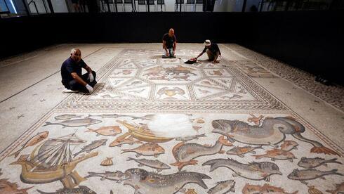 Los trabajadores limpian un mosaico de la época romana restaurado después de ser expuesto en su emplazamiento original en Lod.
