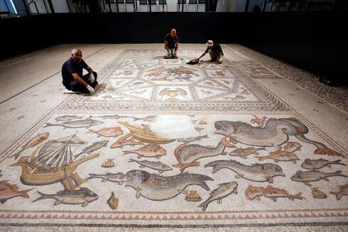 Los trabajadores limpian un mosaico de la época romana restaurado después de ser expuesto en su emplazamiento original en Lod.