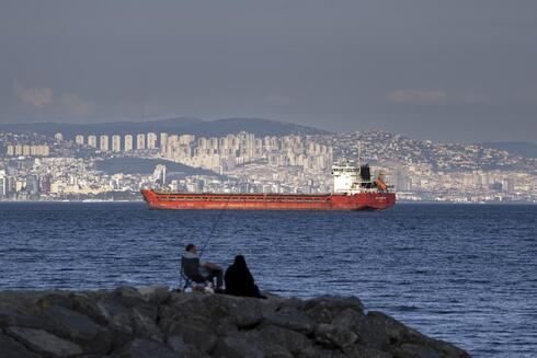 Una familia sentada en una roca frente a un buque de carga anclado en el Mar de Mármara espera el acceso para cruzar el Estrecho del Bósforo en Estambul, Turquía, el 13 de julio de 2022. 