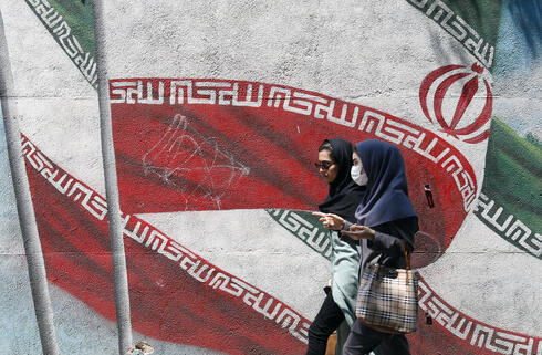 Mujeres iraníes pasan junto a una pintura mural de la bandera nacional de Irán en una calle del centro de Teherán.