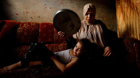 Una mujer palestina abanica a su hija con una bandeja en medio de la ola de calor y los prolongados cortes de electricidad.