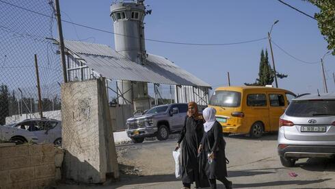 Los palestinos pasan por delante de una torre de vigilancia militar israelí con dos armas robóticas y cámaras de vigilancia en el campo de refugiados de Aroub, en Cisjordania, el jueves 6 de octubre de 2022.