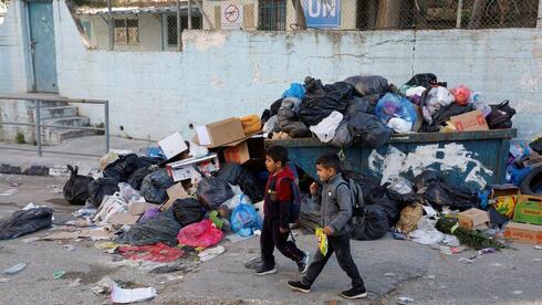 Niños palestinos pasan junto a un montón de basura en el campo de refugiados de Al Jalazone, cerca de Ramala, en Cisjordania, el 25 de enero de 2023. (Reuters) Niños palestinos pasan junto a un montón de basura en el campo de refugiados de Al Jalazone, cerca de Ramala, en Cisjordania, el 25 de enero de 2023.